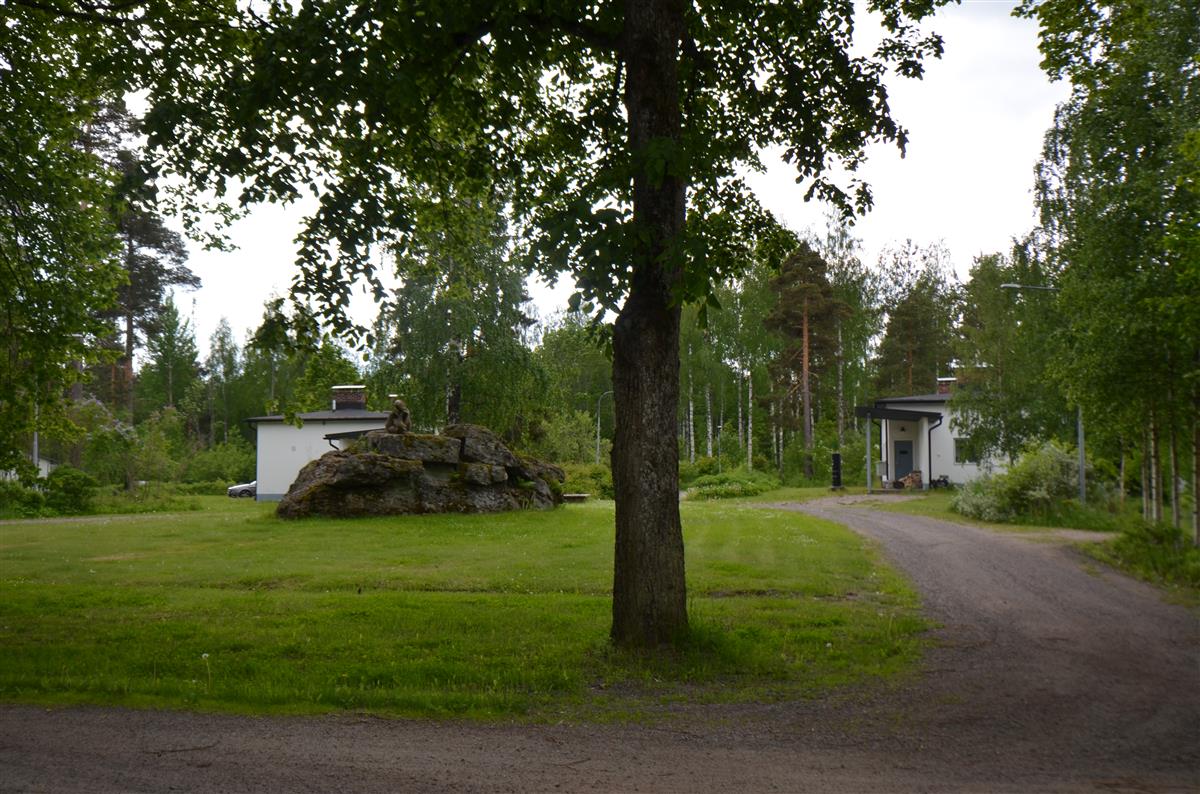 Näkymä Lättäläntieltä kaakkoa kohti. Puistoalueella, luonnonkiven päällä on Gunnar Finnen veistos Leikkivä nalle. Taustalla Lättälänkaari 3:n ja 5:n asuinrakennukset.&nbsp;(Päivi Makkonen&nbsp;2025)