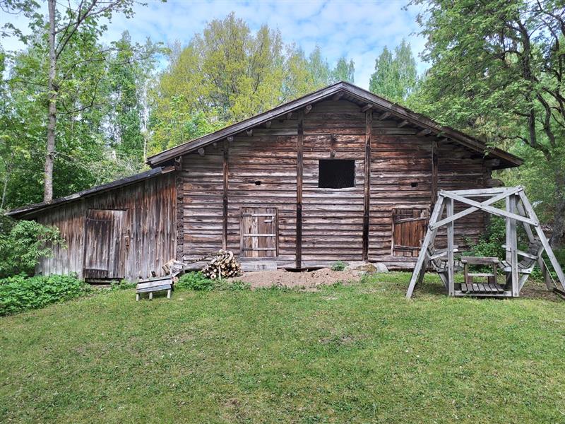 Maalaamattomasta hirsisestä pääosasta ja matalammasta laudoitetusta sivusiivestä koostuva aittamainen talousrakennus.&nbsp;(Dan Ronimus&nbsp;5/2022)