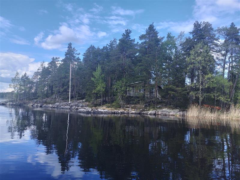Saunasta ja uudemmasta asuinrakennuksesta katsoen niemenkärjen toisella puolen sijaitseva alkuperäisen rakennusvaiheen asuinrakennus.&nbsp;(Dan Ronimus&nbsp;5/2022)