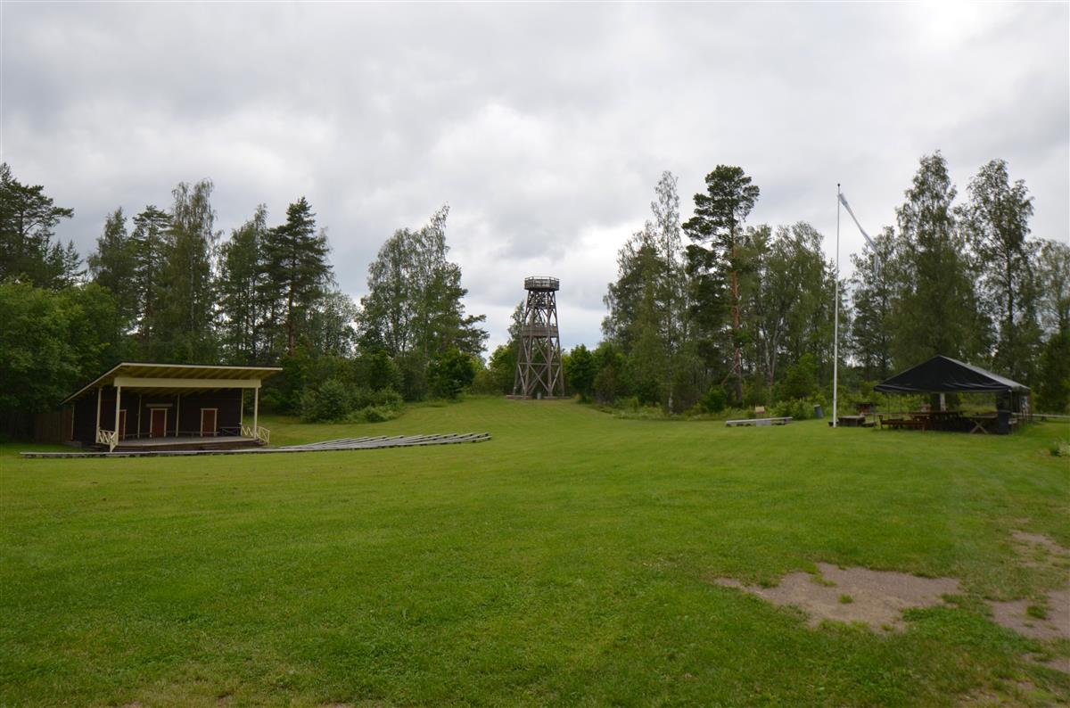 Hakamäen museoalueen näkötorni kaakosta päin kuvattuna. Vasemmalla esiintymislava katsomoineen. [Kohteen rakennukseen liitetty kuva]&nbsp;(Päivi Makkonen&nbsp;2025)
