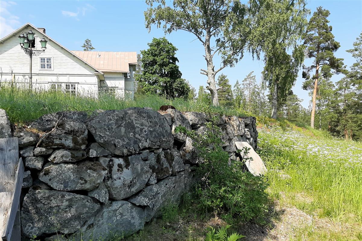 Ruhtinaan majan eteläpuolen pihan huvila-aikaista kivipengerrystä ja maakellarin paikka lounaasta päin kuvattuna. Kellarin ovi lienee aiemman Partakosken redutin kulkuaukon kohdalla.&nbsp;(Esa Hertell&nbsp;17.6.2020)