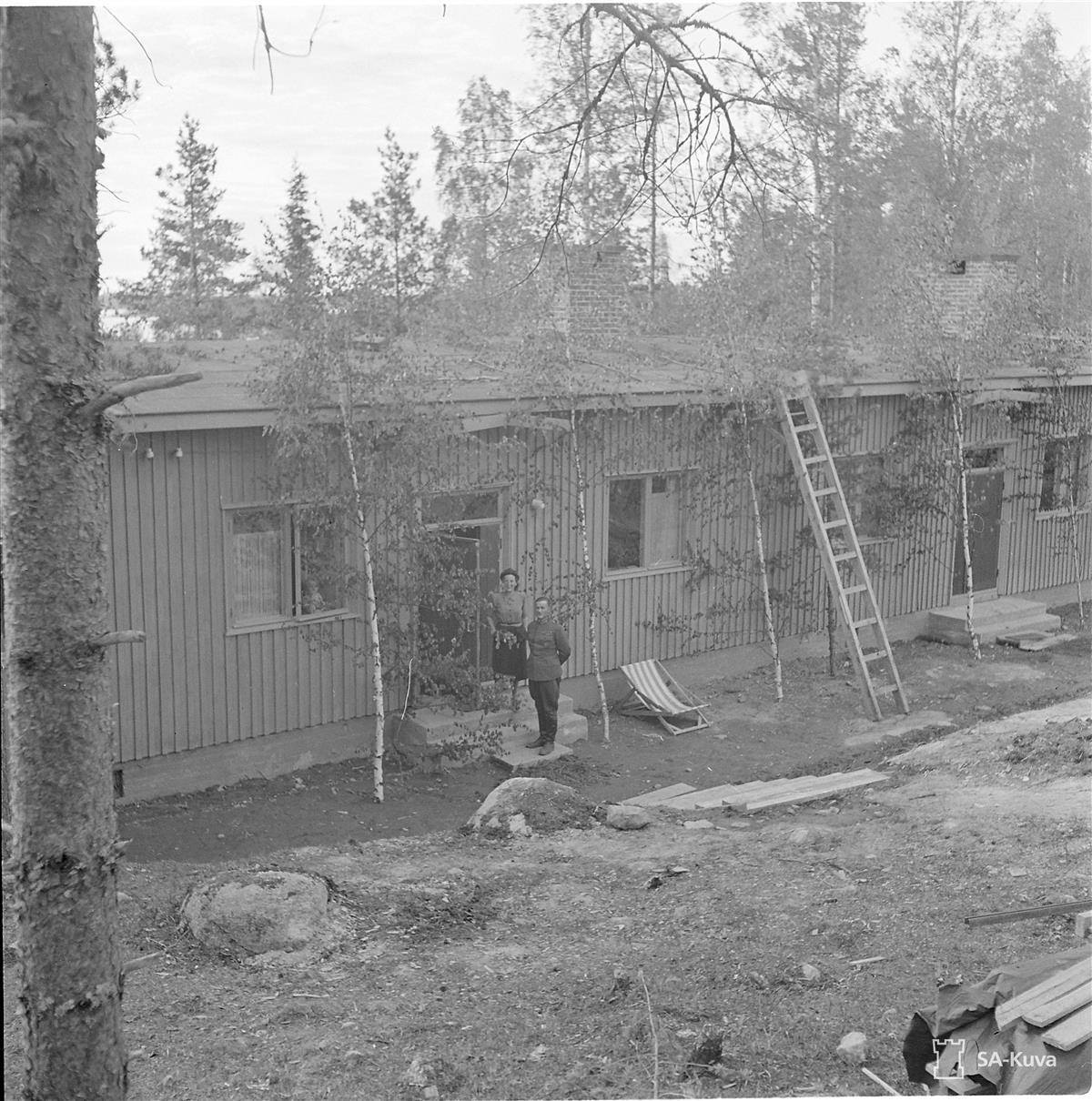 SA-kuva upseeriparakista Lemin Kantturaniemestä 24.6.1941. Portailla asukkaat eversti Lauri Maskula ja puolisonsa laulaja ja näyttelijä Ritva Aro sekä pikkulotta Maija-Liisa Maskula ja karkeakarvainen taistelulähetti Priha.&nbsp;(SA-kuva&nbsp;1941)