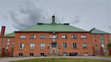 Kuva: Kansliarakennuksen julkisivu ulkopihalta kuvattuna. Taustalla selli- ja hallintorakennukset.&nbsp;(Dan Ronimus&nbsp;6/2022)